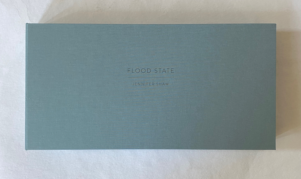 Rectangular portfolio box covered in blue cloth with the title "FLOOD STATE - Jennifer Shaw" stamped on the front in subtle letters.