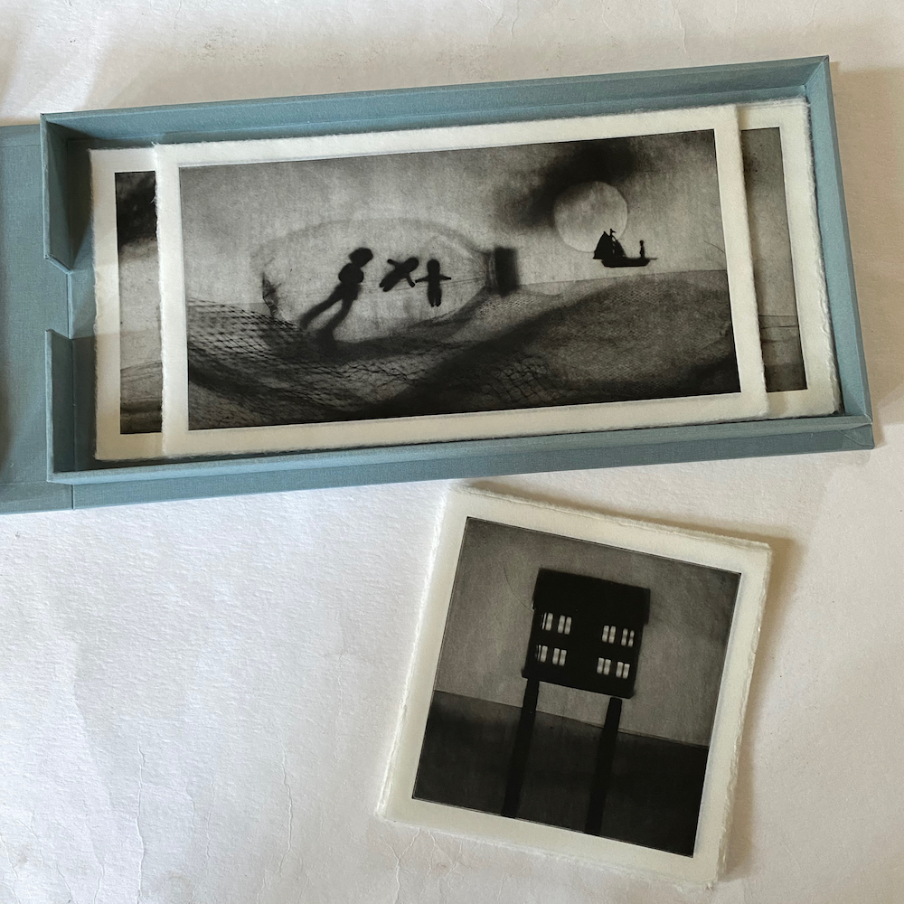 Portfolio open with b&w photogravure prints inside. 6x15" and 6x12" prints are inside the box, with a stack of 6x6" prints outside.